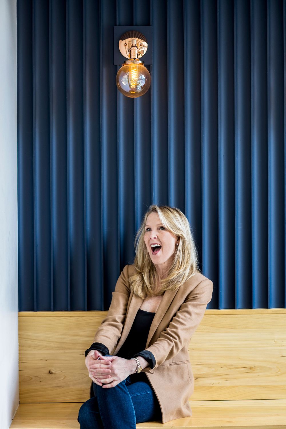 Person laughing while sitting on wooden bench against blue paneled wall with pendant light.