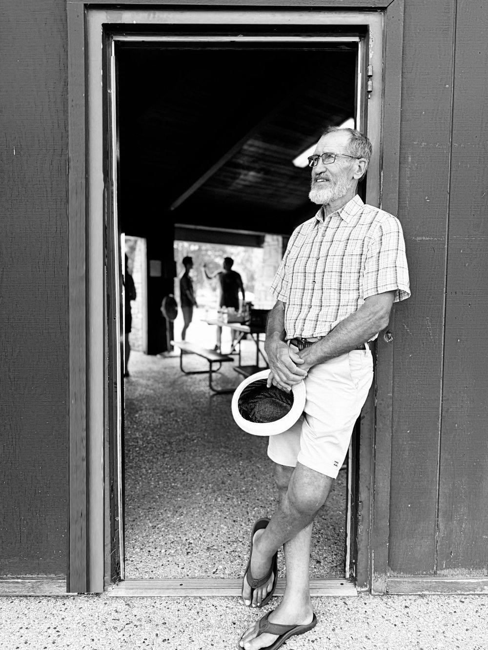Elderly person in plaid shirt and shorts standing in doorway of barn.