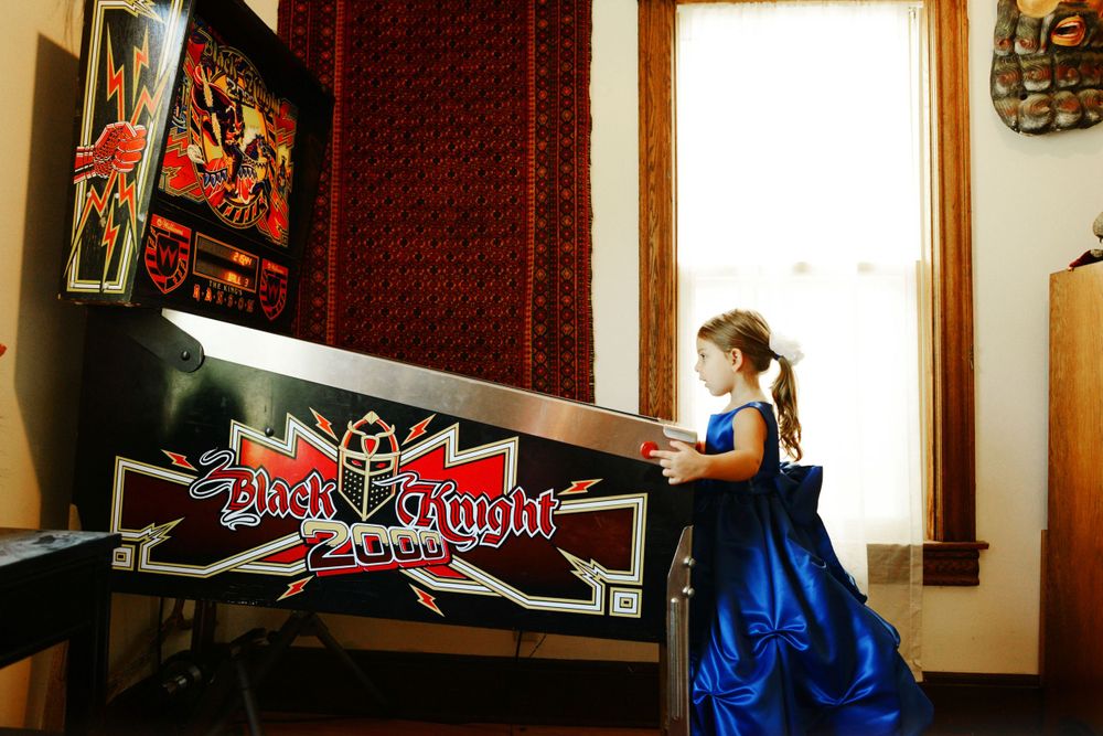 Blue-dressed figure plays arcade game in room with red tapestry wall.