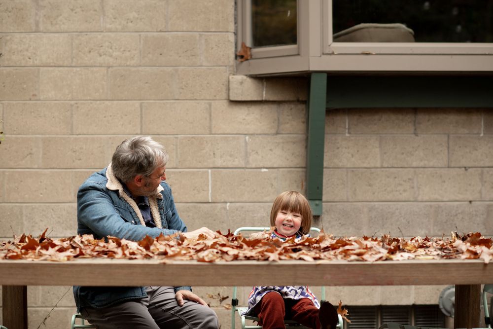 Fall scene with people sitting at outdoor bench covered in autumn leaves.