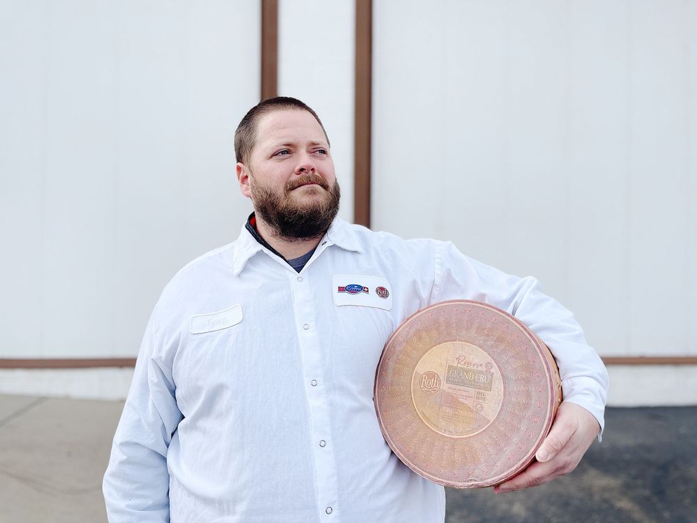 Chef in white uniform holding a copper plate against white wall background.
