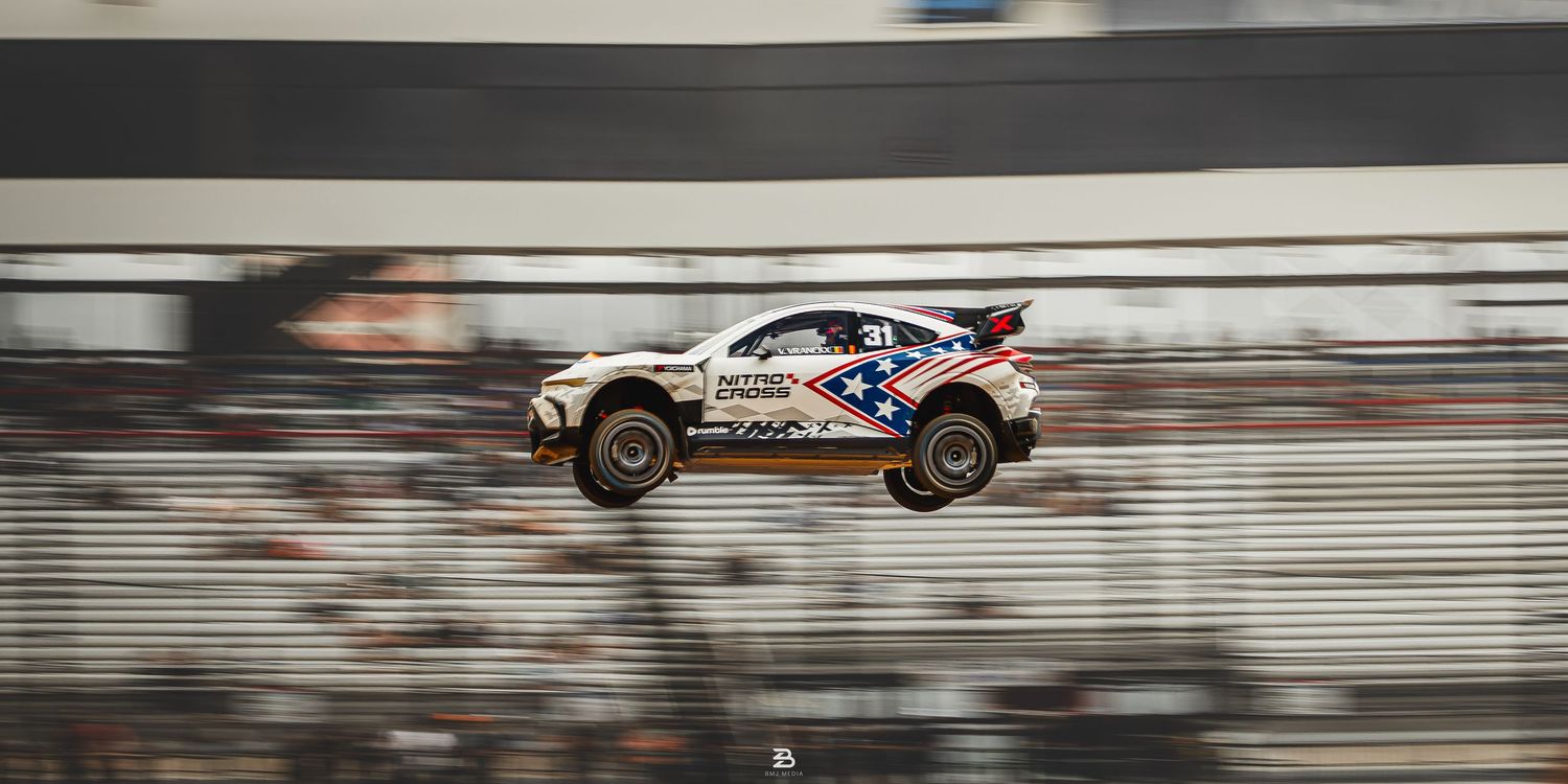 White Dodge Hornet airborne after clearing a dirt ramp at Nitrocross