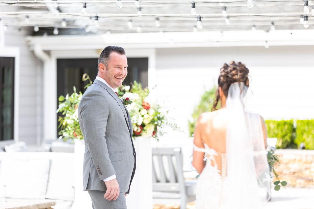 A first look moment between a couple at an outdoor wedding venue with white floral arrangements.