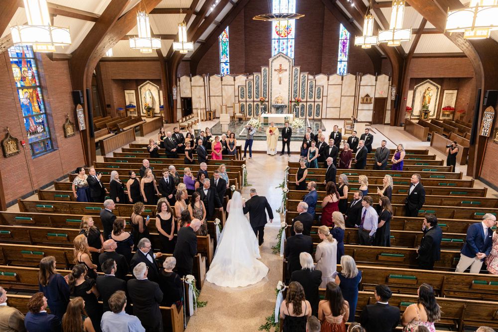 Overhead view of a wedding ceremony in a church with guests seated in wooden pews.
