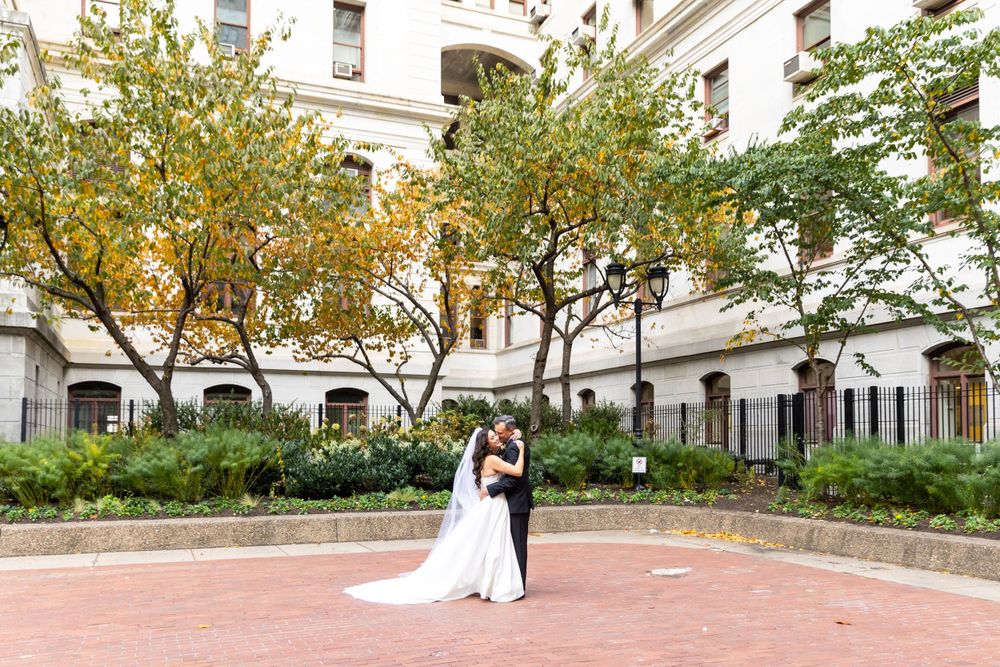 Bride and groom share an intimate moment in a classic architectural courtyard with fall trees.