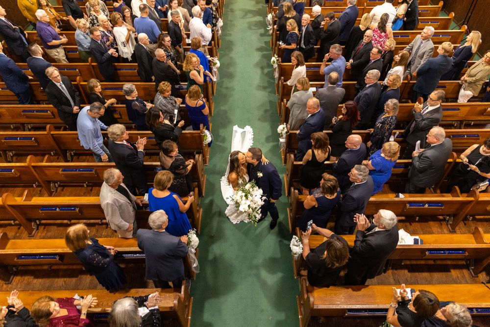 Bird's eye view of a wedding ceremony in a church with wooden pews and emerald green carpeting.