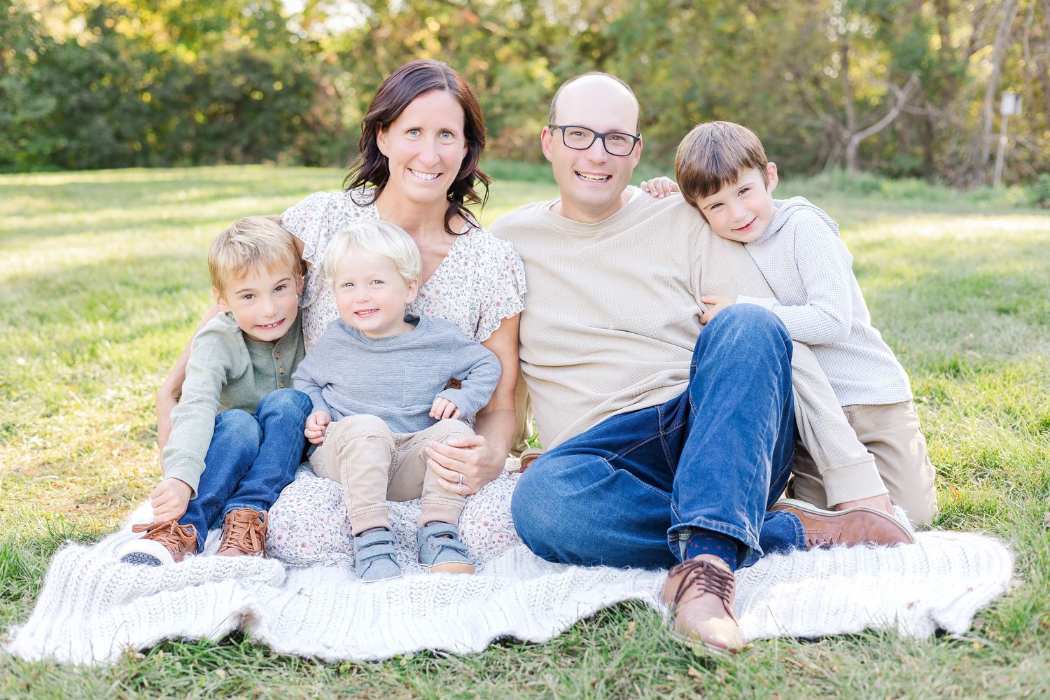 Family group relaxing together outdoors on white blanket during golden hour photo session.