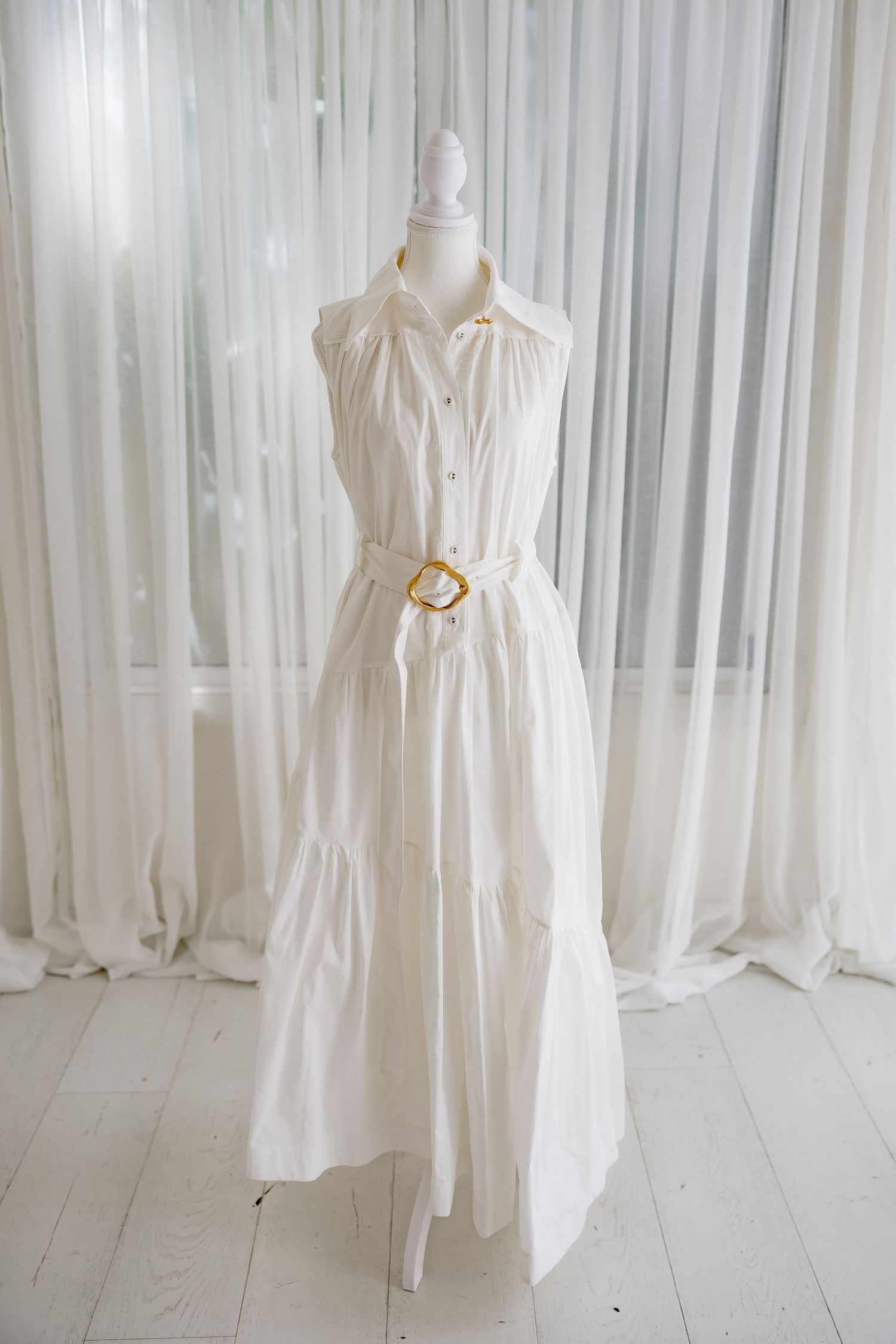 Classic white sleeveless dress with collar and gold belt buckle displayed on mannequin.