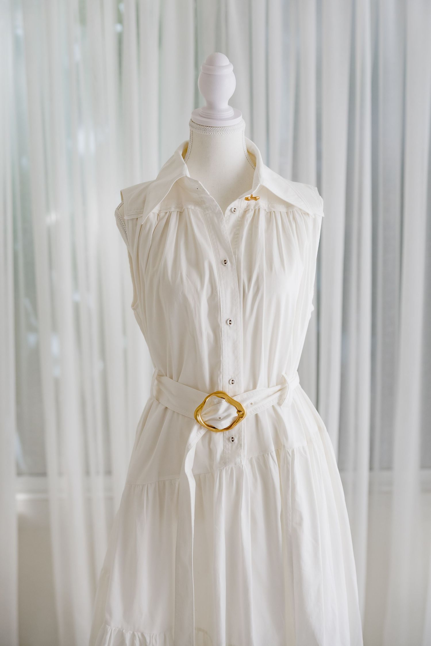Elegant white button-up dress with gold circular belt detail shown on dress form.