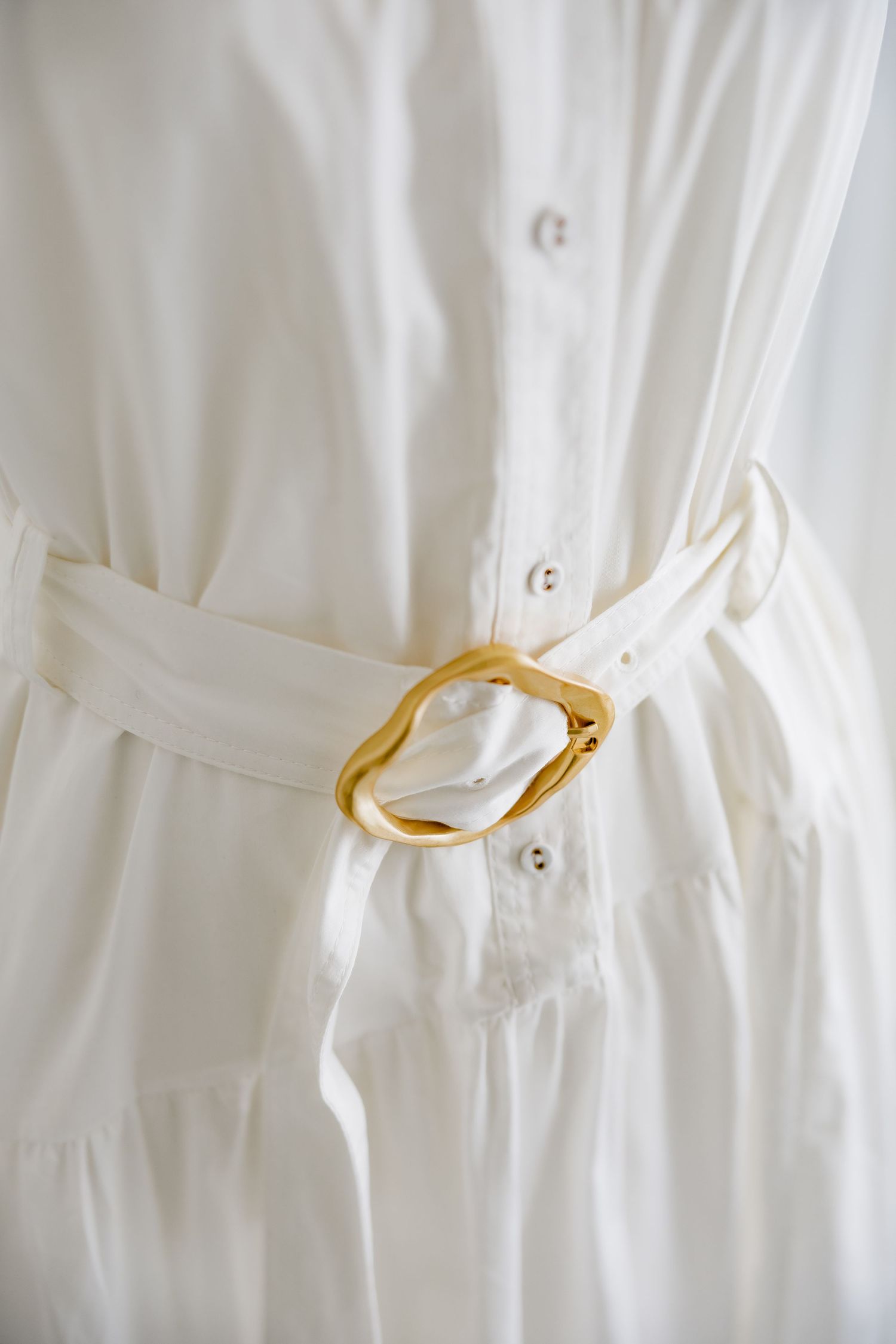 Close-up detail of a white dress showing a gold buckle belt cinching the waist.