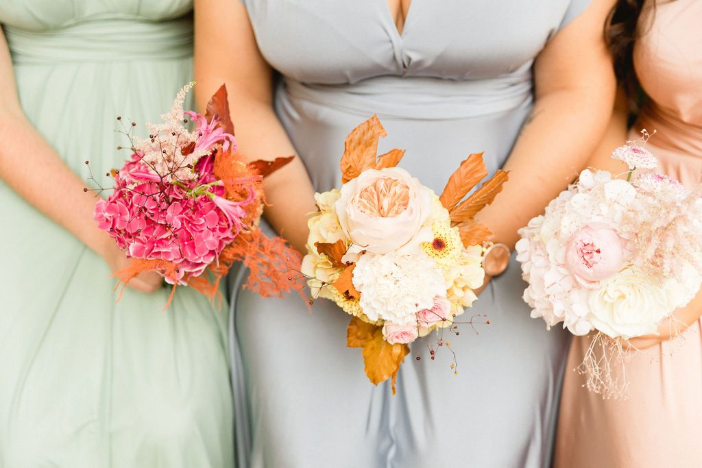 A row of wedding party members holding colorful pink and peach floral bouquets against light gray dresses.