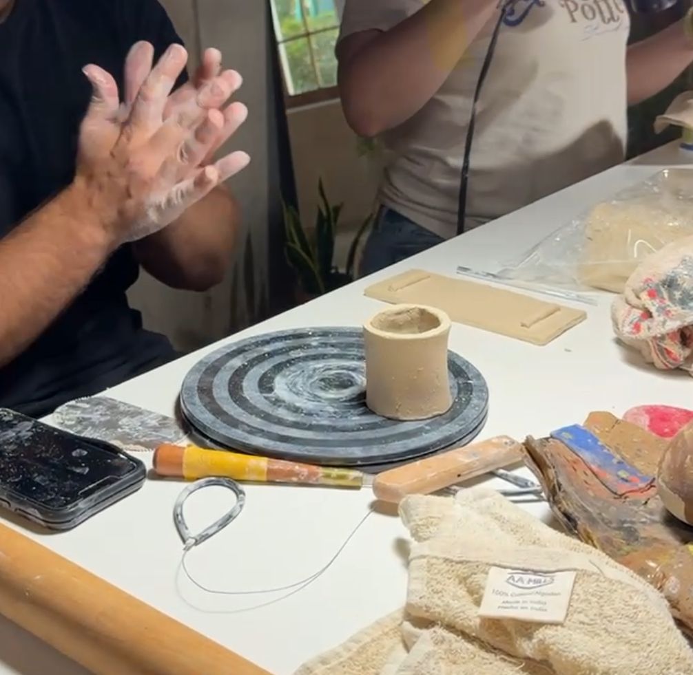 Pottery instructor demonstrating clay throwing techniques at a wheel during a hands-on studio class.