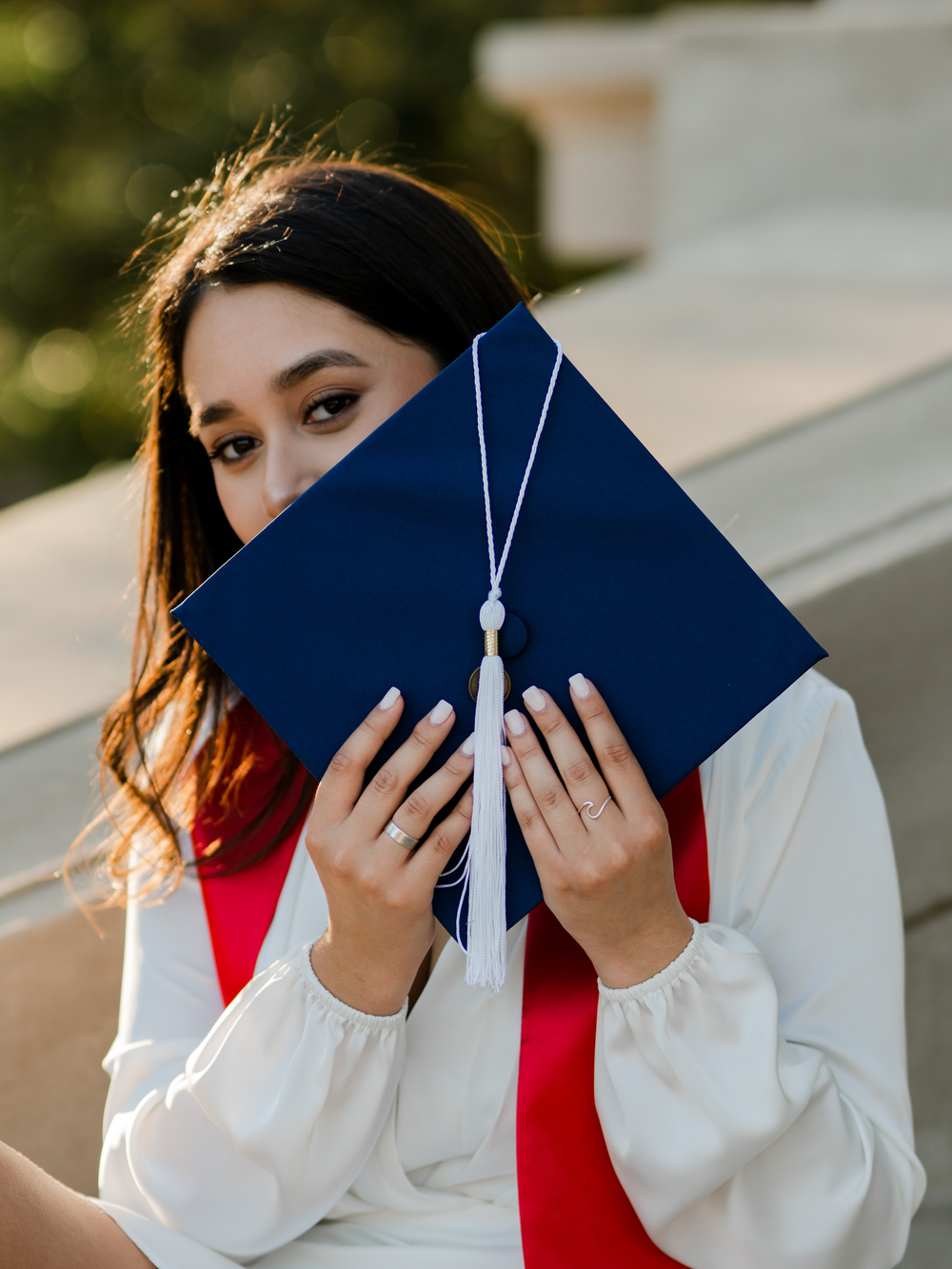 Graduate holds blue diploma cover with white tassel while wearing red graduation stole.