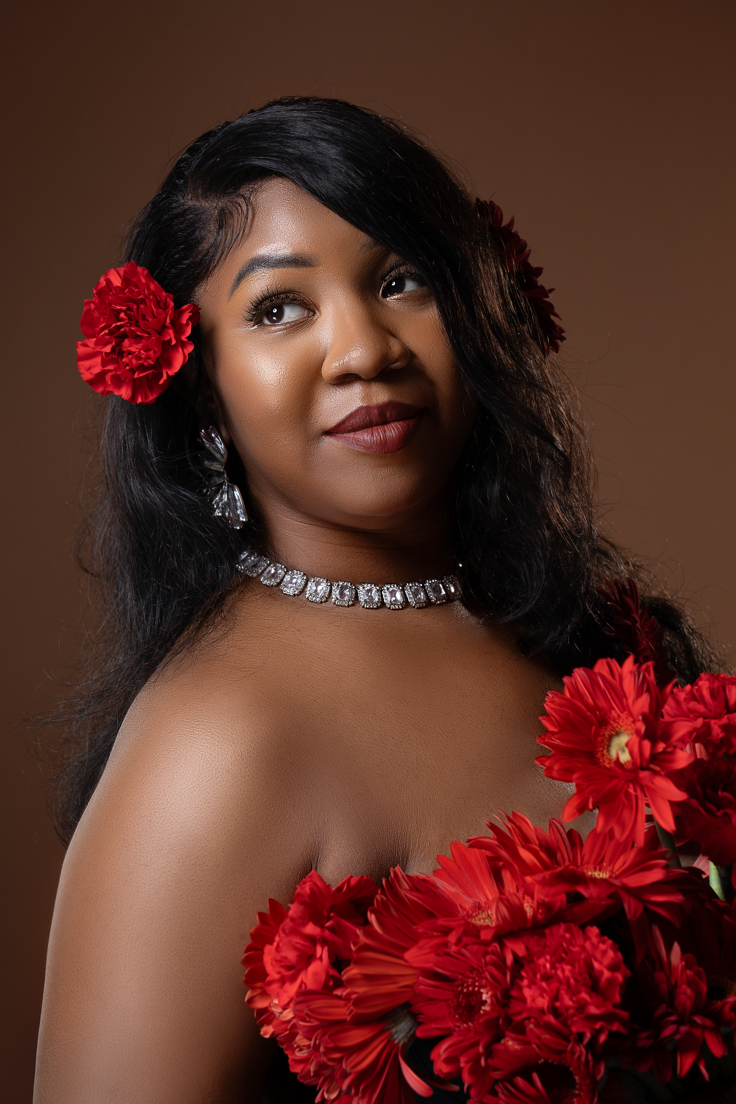 Glamour portrait with red flowers and crystal necklace against brown background.