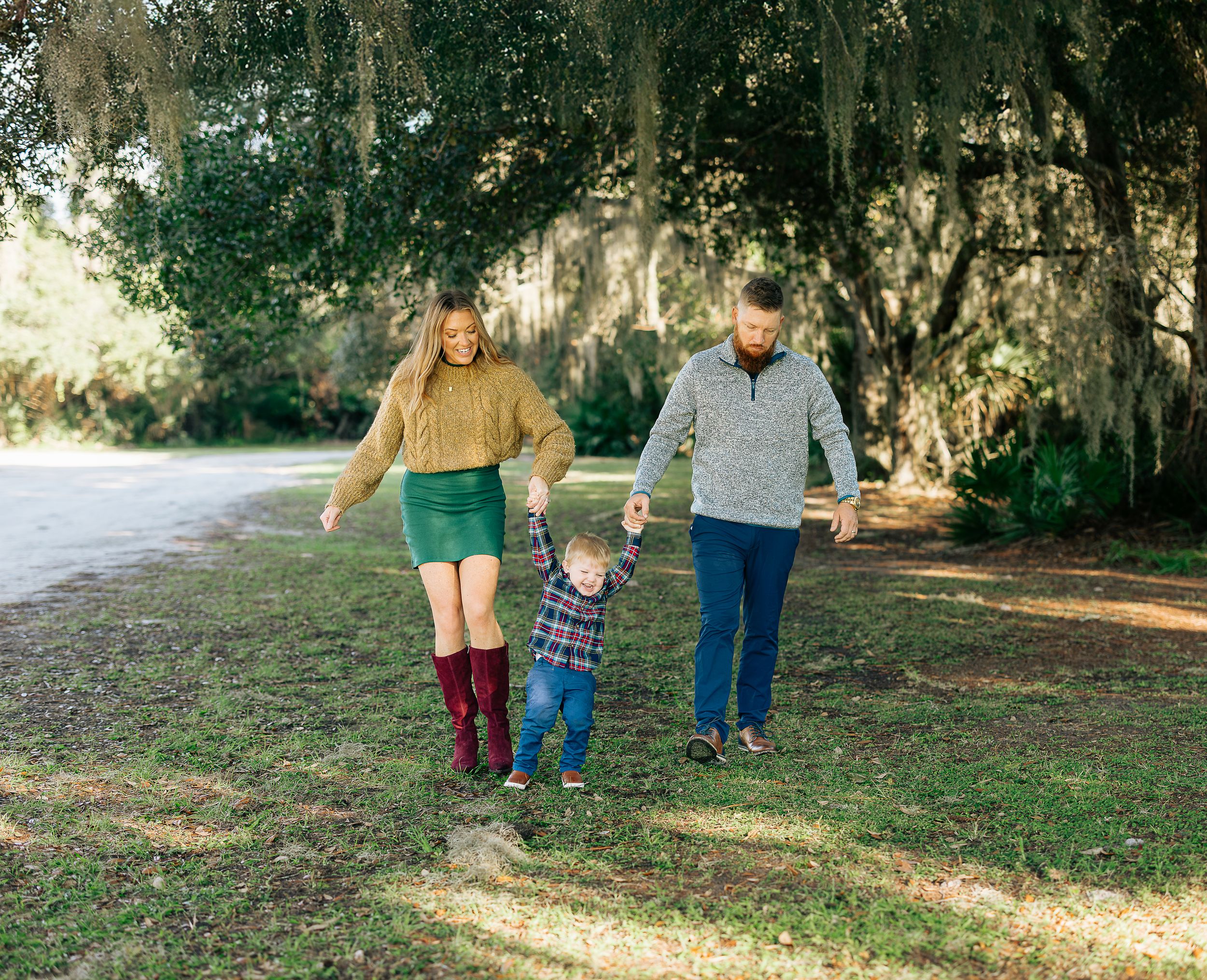 A family walks together on a tree-lined path on a sunny afternoon.