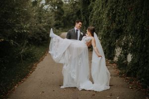 A couple shares a romantic moment on a tree-lined path as the bride's elegant white veil flows in the breeze.