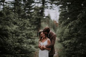 An intimate moment captured between two people embracing on a forest path surrounded by evergreen trees.