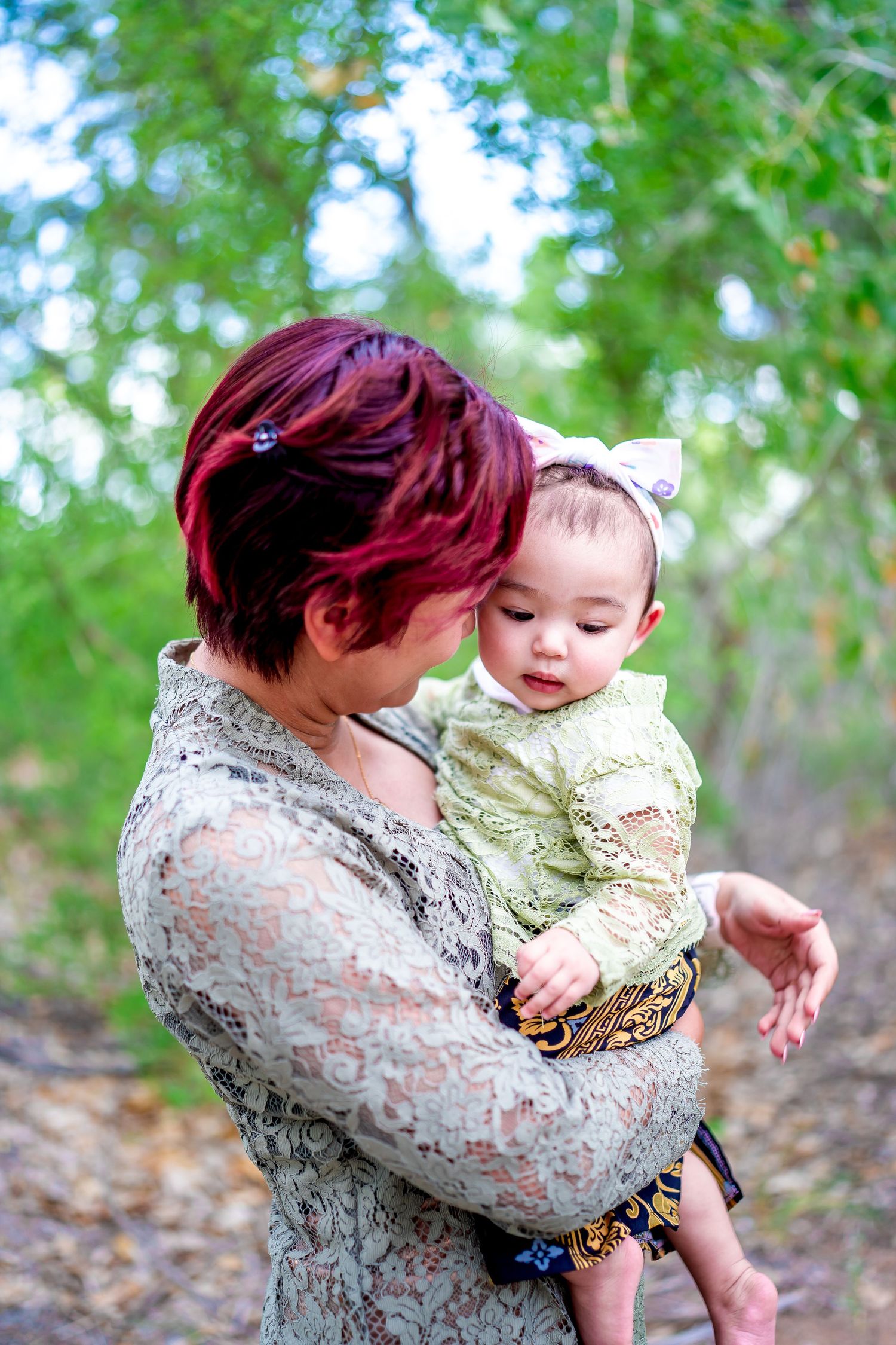 A tender moment between parent and baby outdoors among green trees.