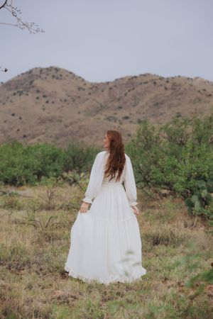 White dress flows gracefully in desert environment with mountains and desert vegetation.