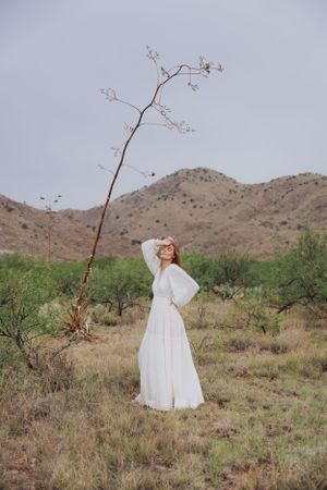 White dress dances in desert wind with mountains and natural vegetation in background.