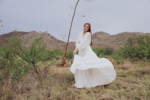 A flowing white dress twirls against a desert mountain landscape with brush and scrub vegetation.
