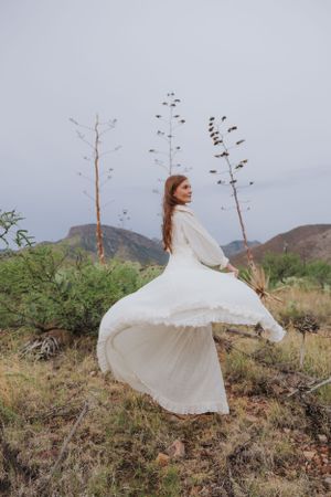 A white dress flows elegantly in the breeze against desert mountains and vegetation.