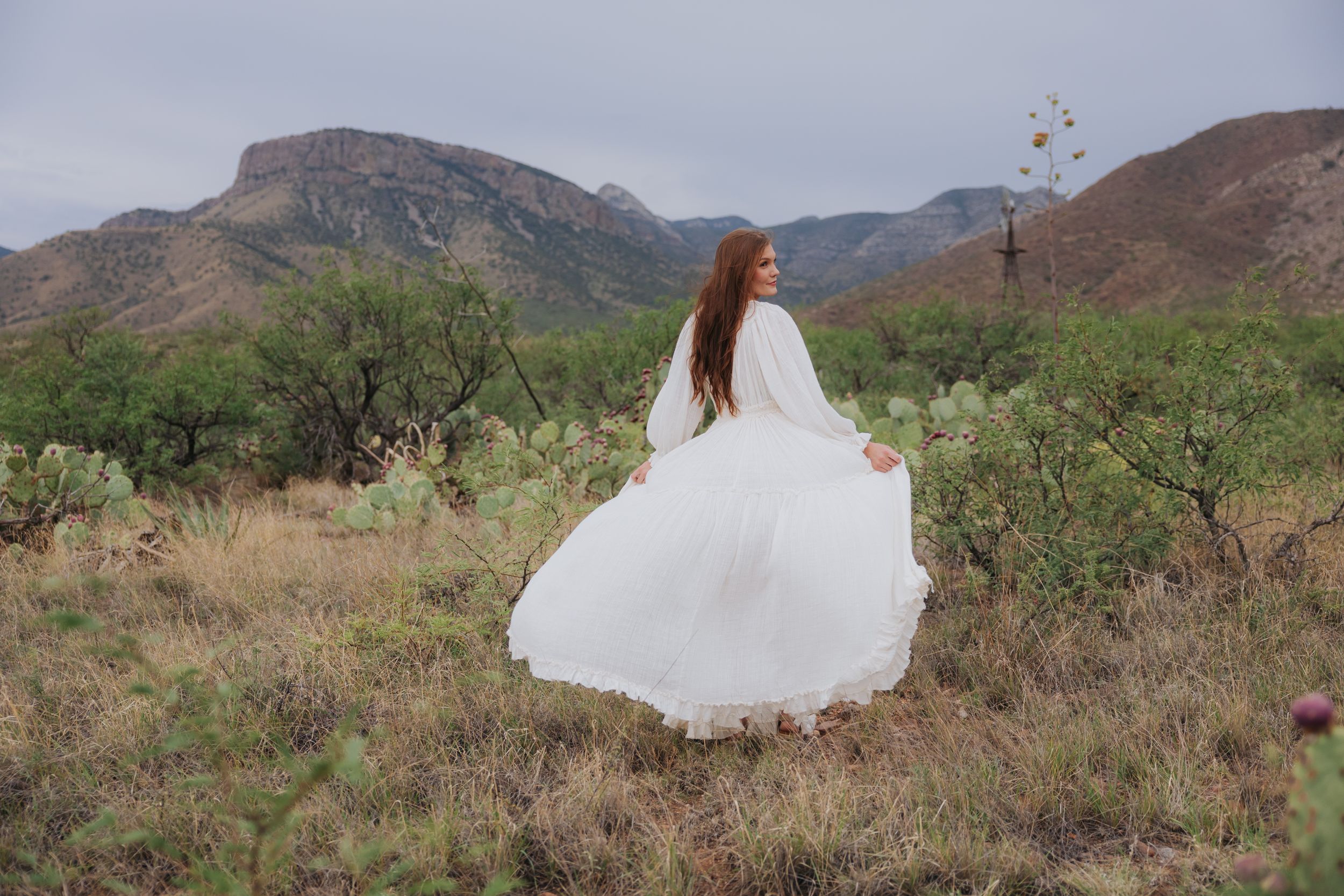 Flowing white gown creates movement against dramatic mountain scenery in a desert setting.