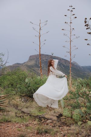 A white dress dances in the wind among desert plants with mountains in the background.