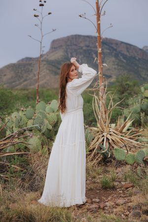 A flowing white dress twirls against a desert mountain landscape with cactus and dry brush.