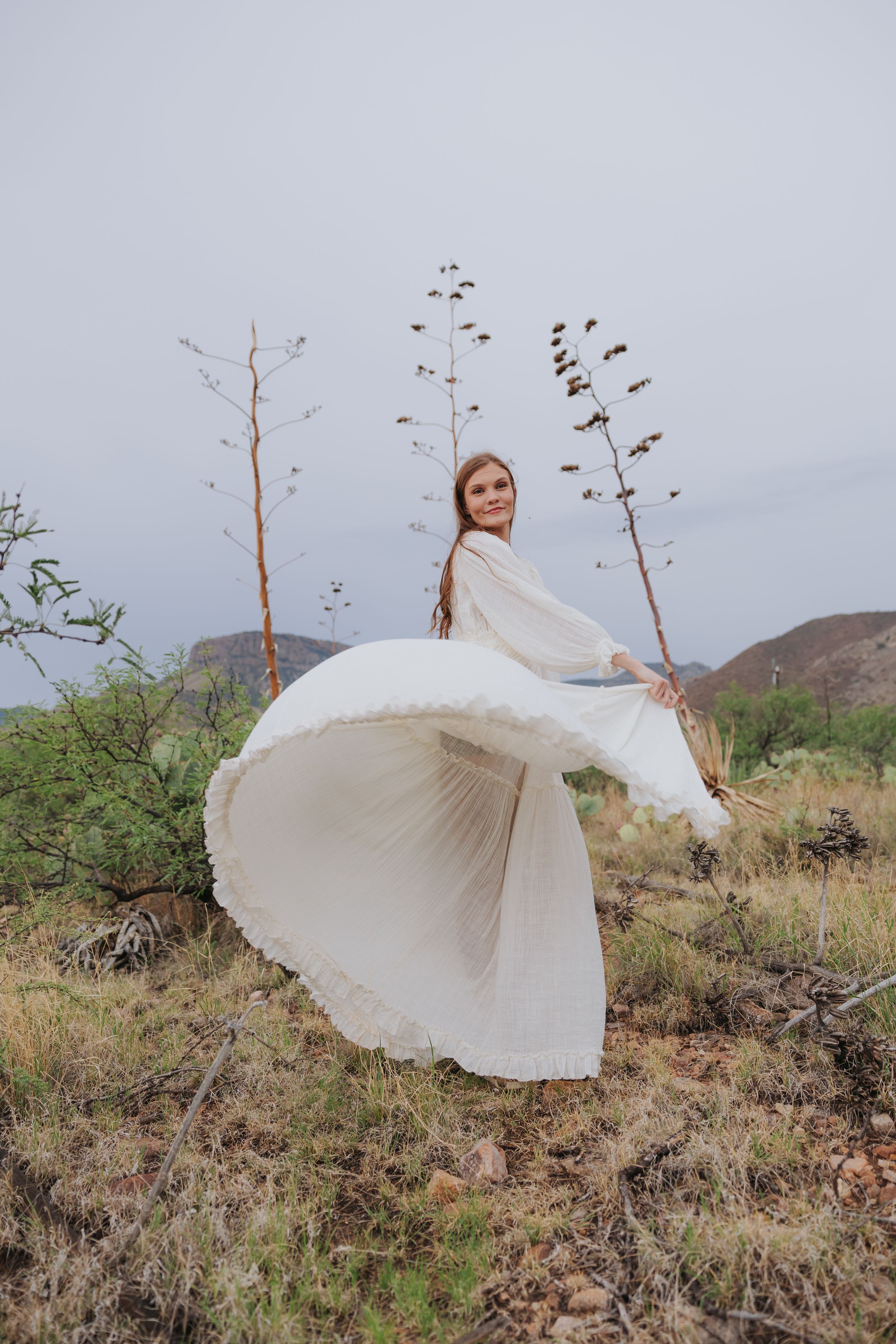 A flowing white dress catches the wind in a desert setting with mountain views.