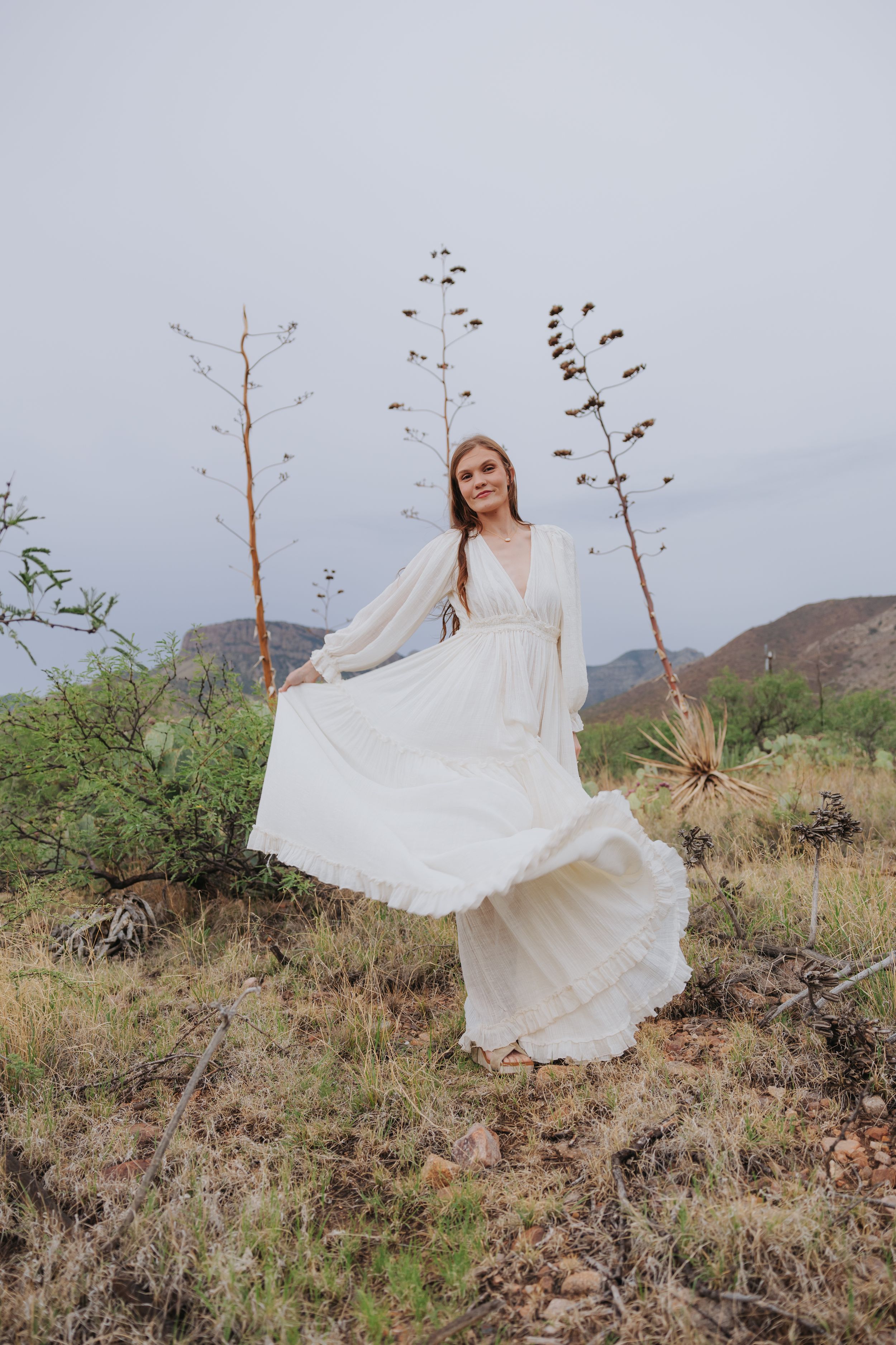 A billowing white dress creates movement against a rugged desert mountain landscape.