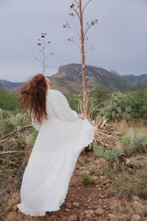 Ethereal white dress billows in the wind against rugged desert terrain and mountain vista.