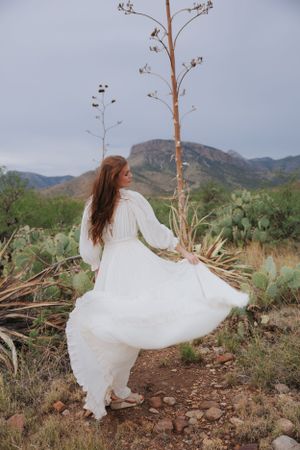 White dress spins dramatically in desert landscape surrounded by cacti and mountains.