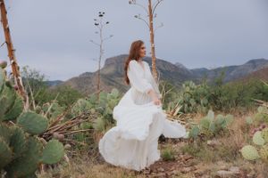 Dreamy white dress twirls in desert setting with mountain backdrop and native plants.