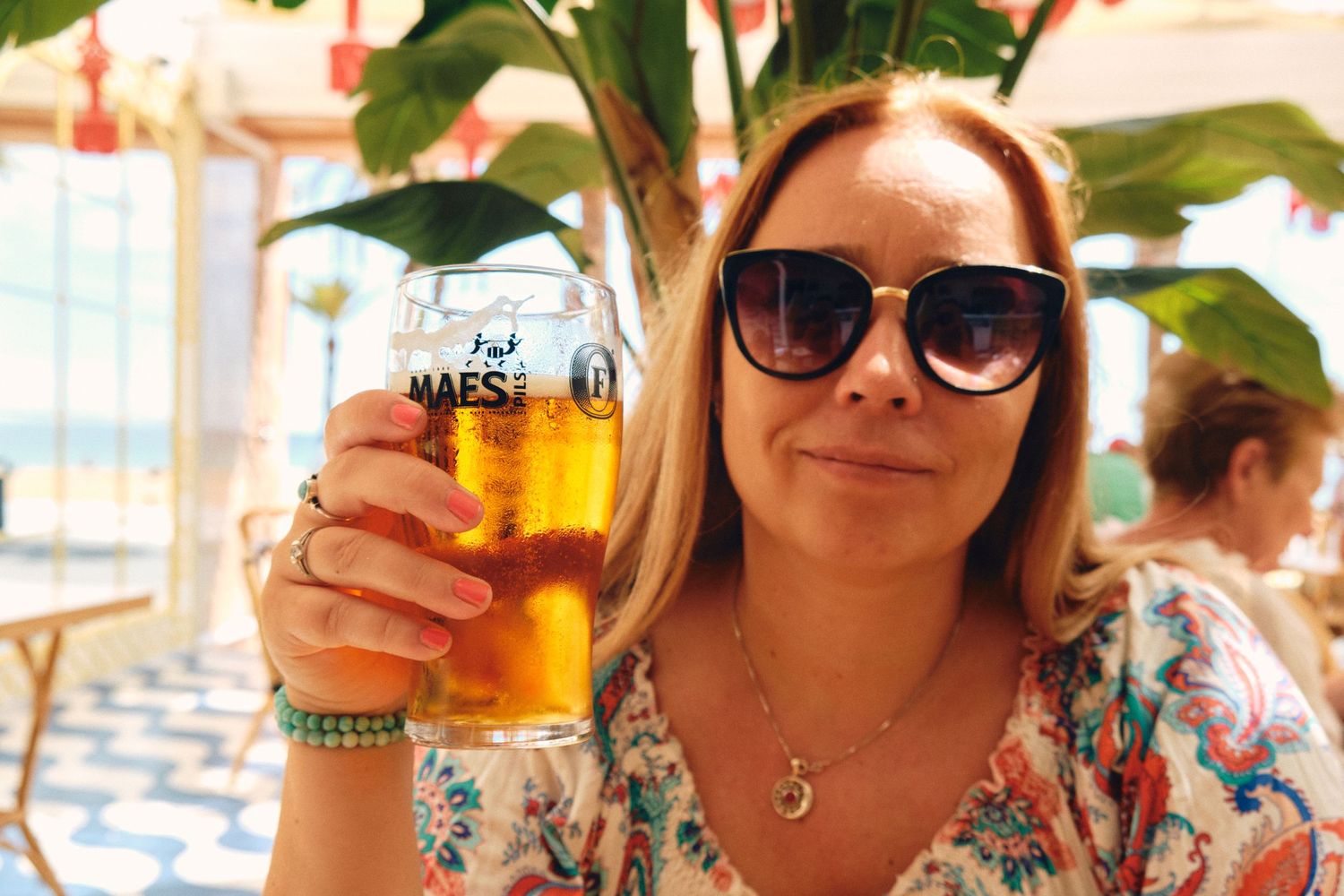 Person holding a large glass of cold beer at an outdoor restaurant.