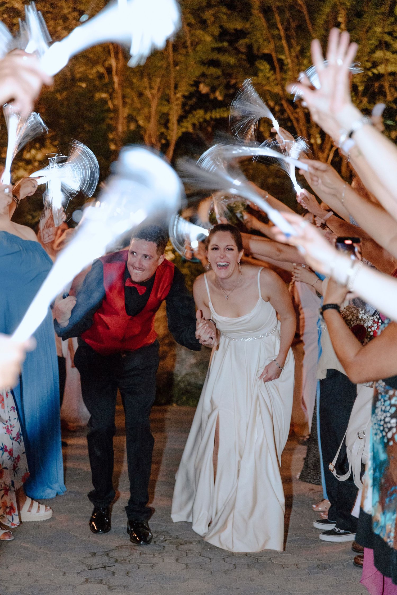 Wedding guests throw white feathers in celebration as couple exits under evening light.