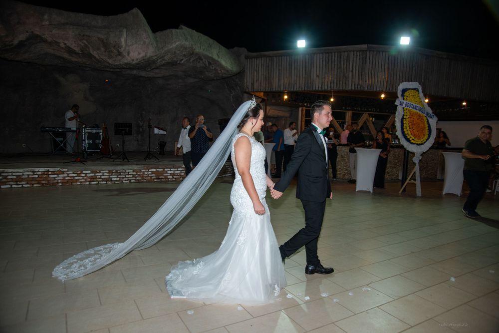 Bride in flowing white gown with long veil walking beside groom at outdoor reception.