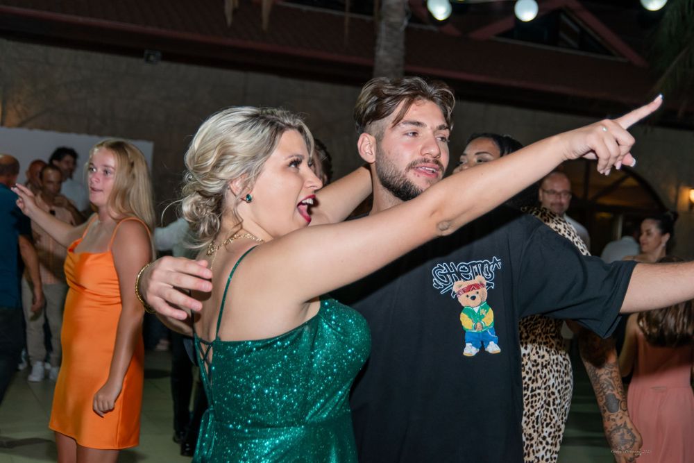 Dancing couple at a party with woman in sparkling green dress pointing while man in black t-shirt looks on.