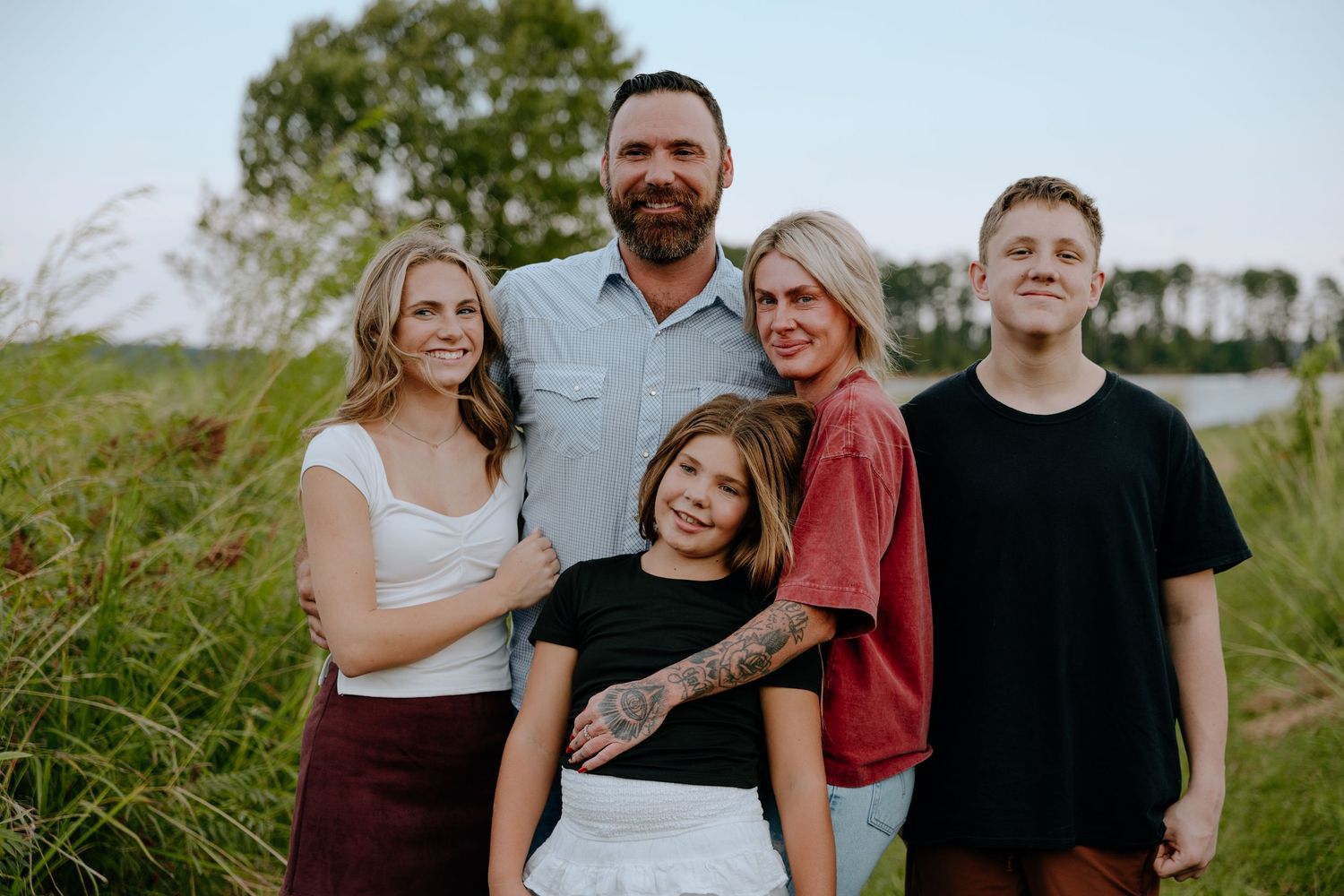 Family group poses together outdoors in casual attire against a natural grassy landscape at sunset in South Carolina