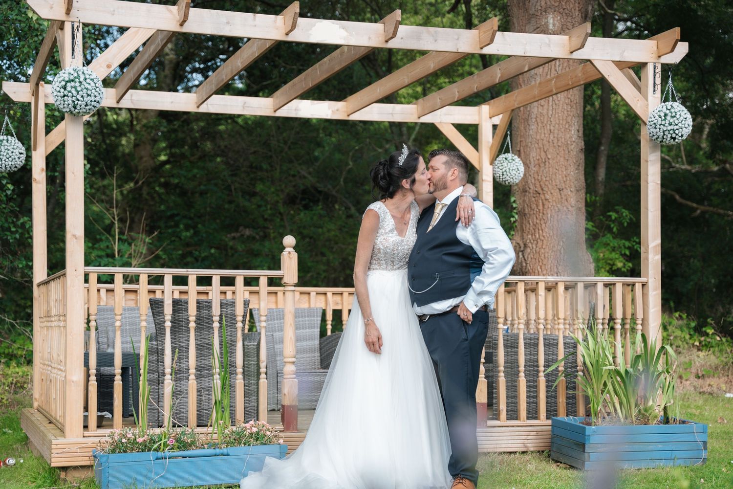 Wedding couple sharing intimate moments under a rustic wooden pergola outdoors.