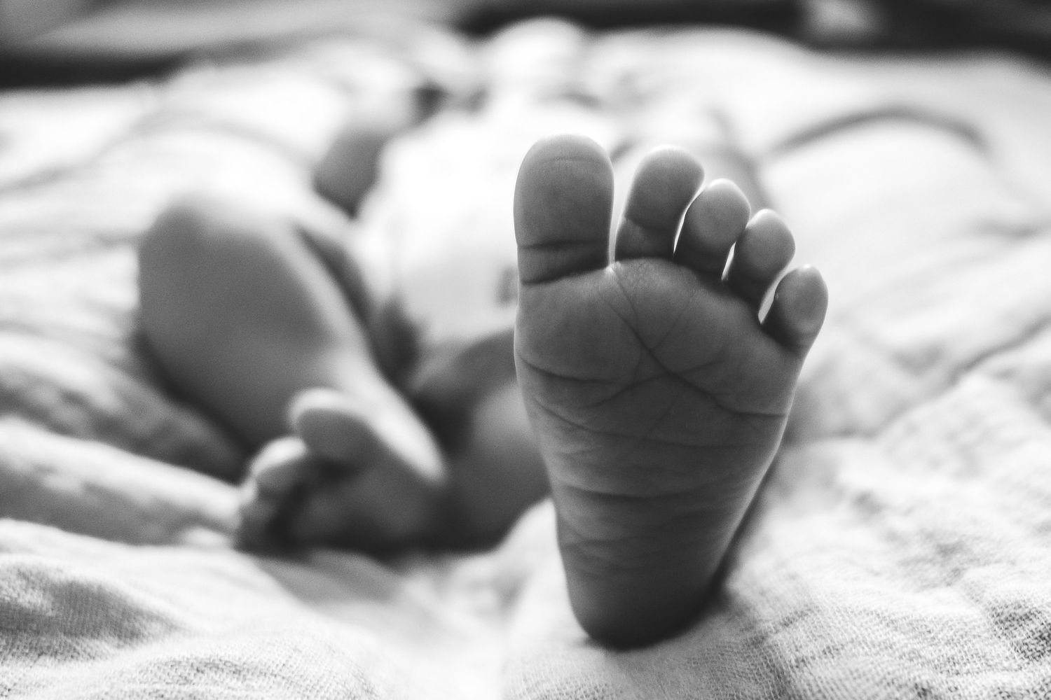 Black and white close-up of a baby's tiny foot on soft bedding.