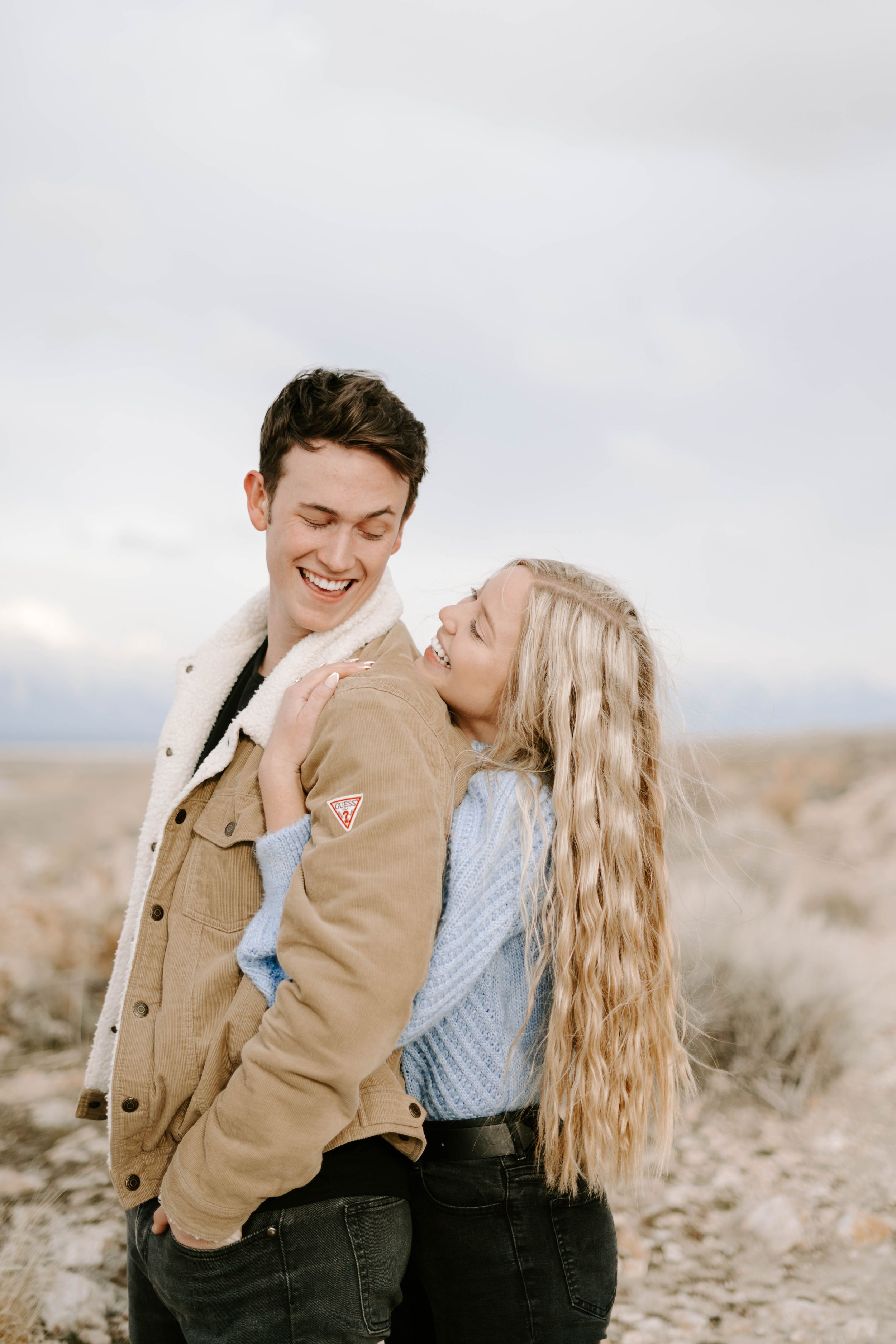 Joyful couple sharing laughter during desert engagement photoshoot.