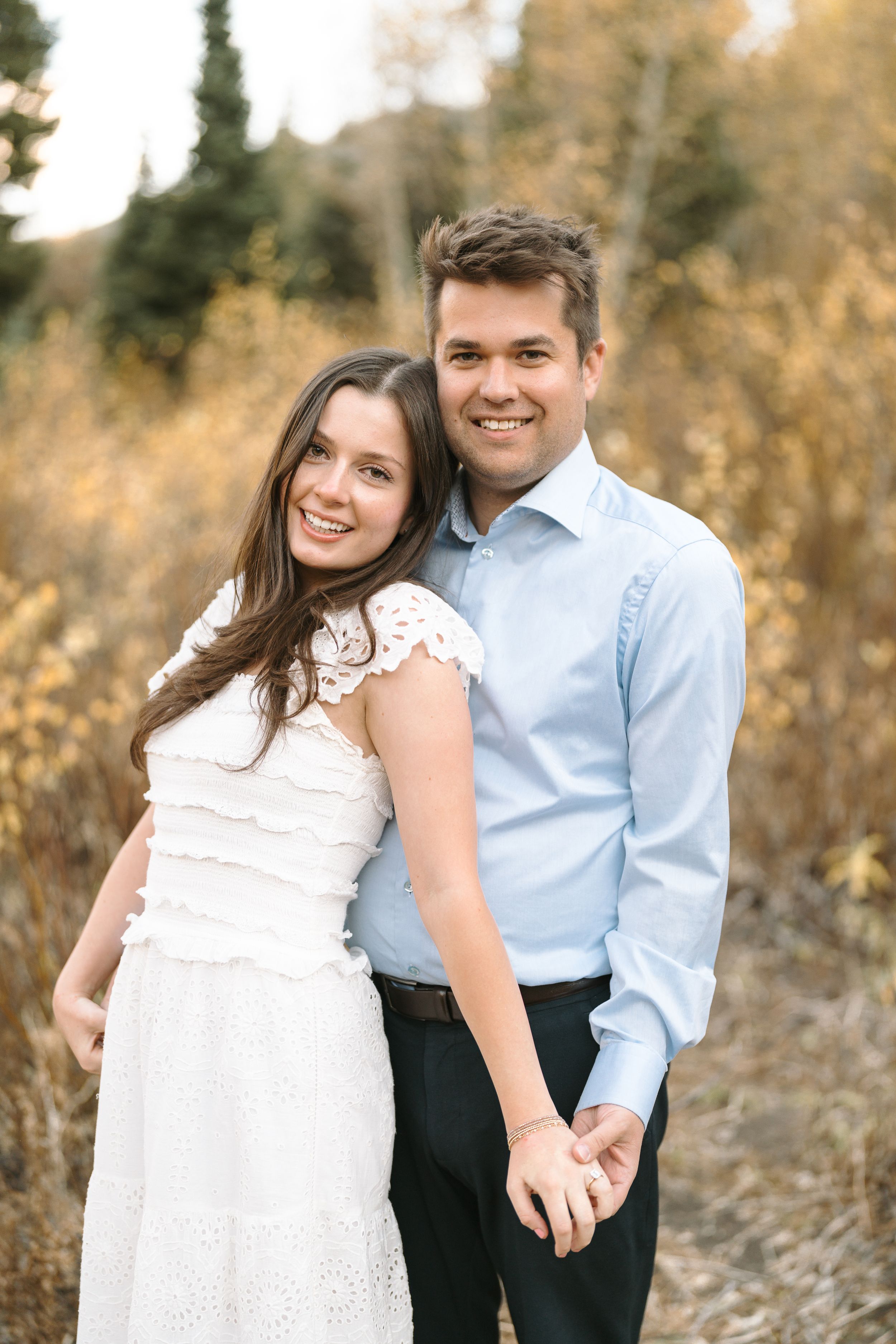 Couple poses together in autumn field wearing formal attire.