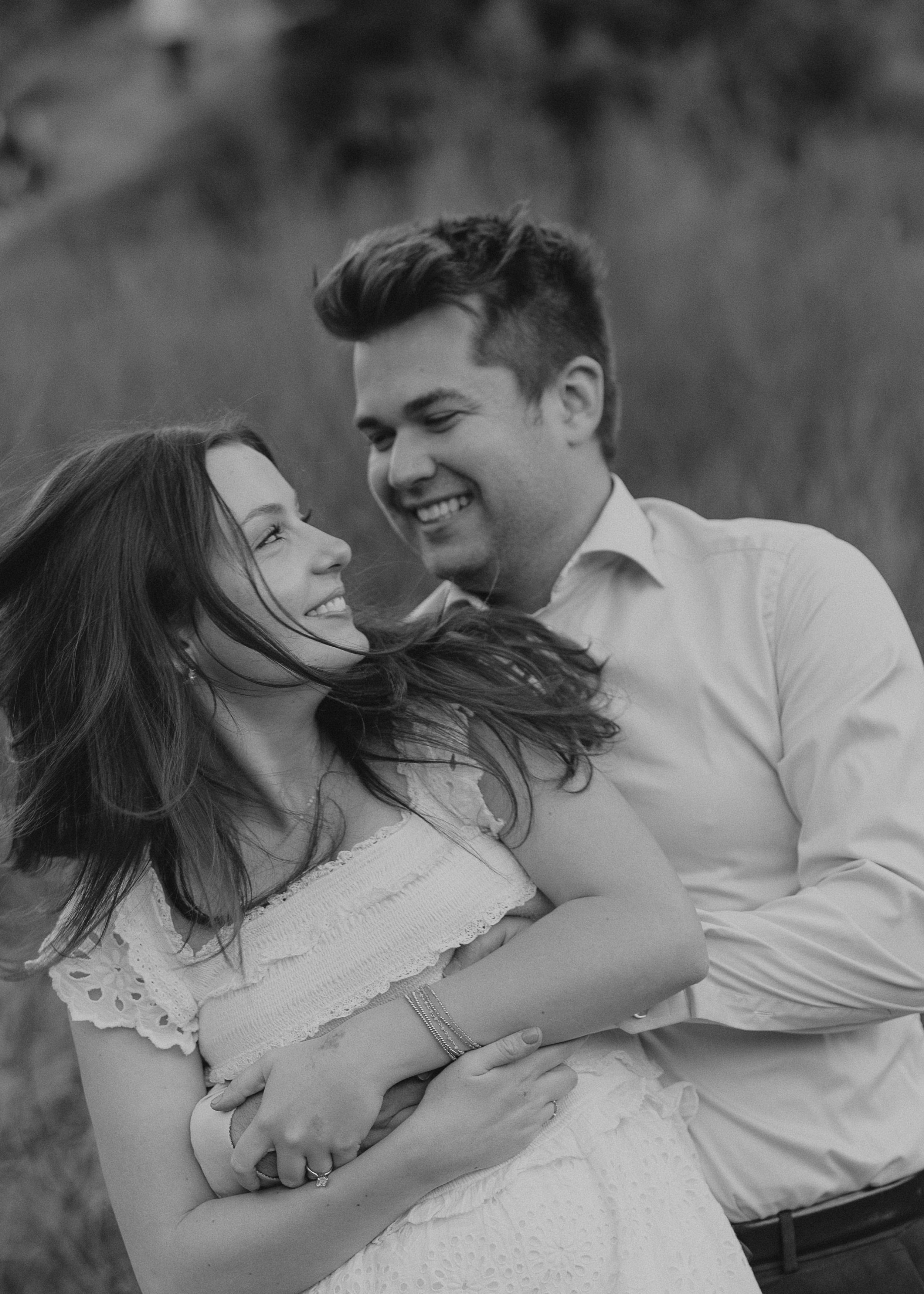 Black and white portrait of couple laughing together in field.