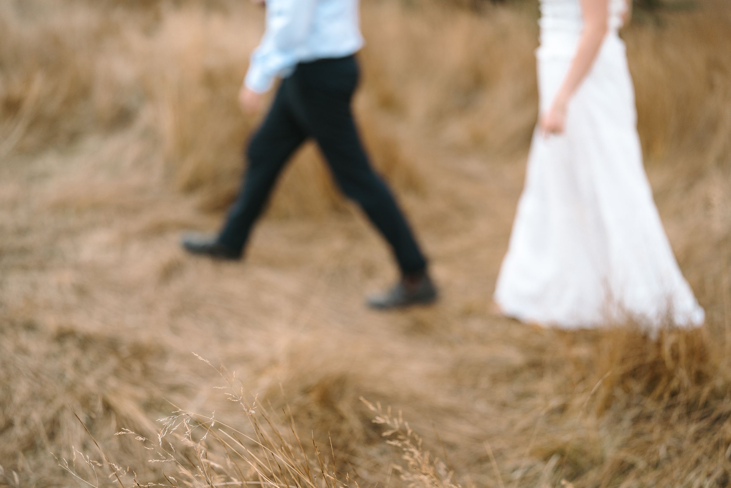 Blurred motion shot of couple walking through tall grass field.