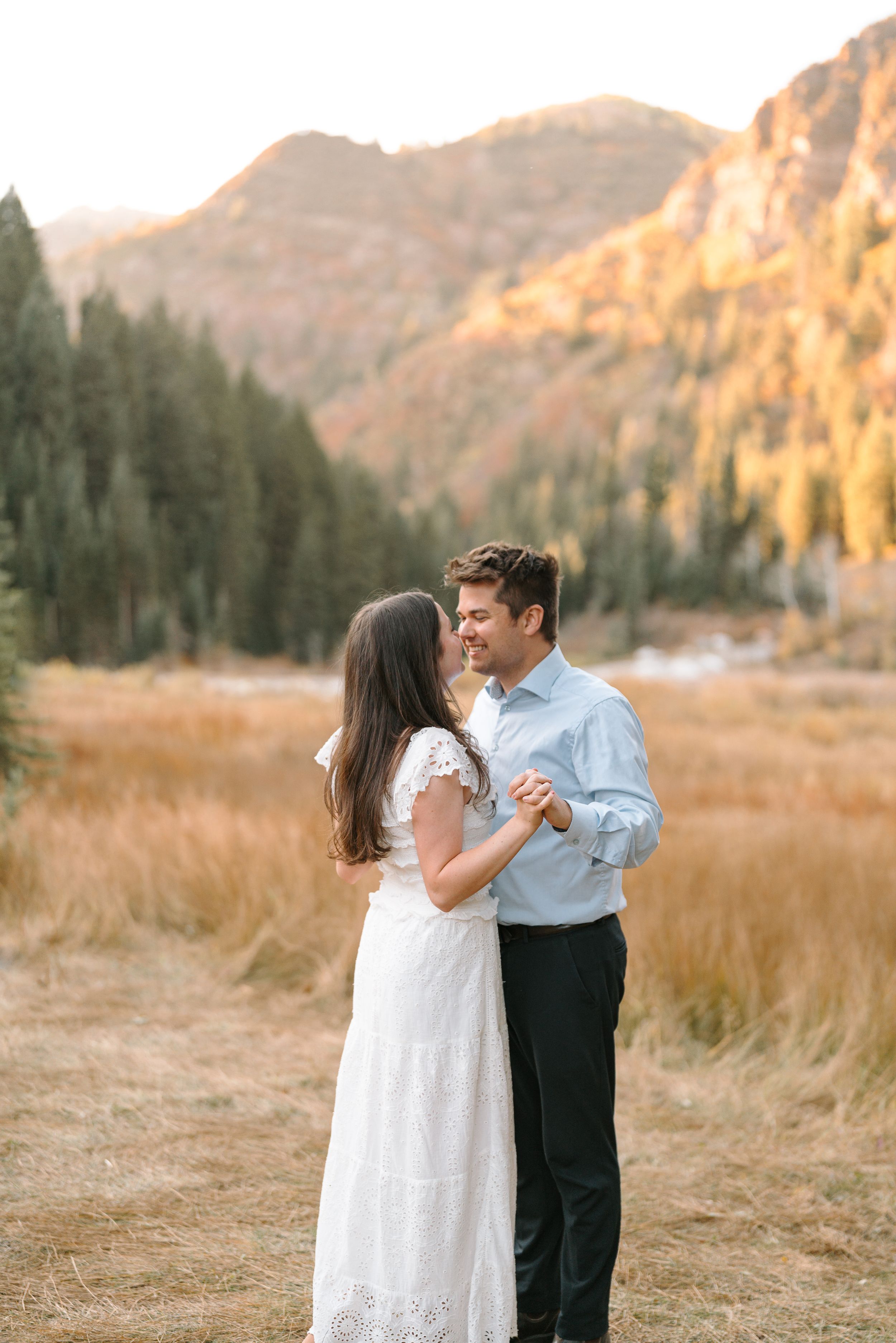 Romantic couple dancing together in a mountain meadow at sunset against rugged cliffs.
