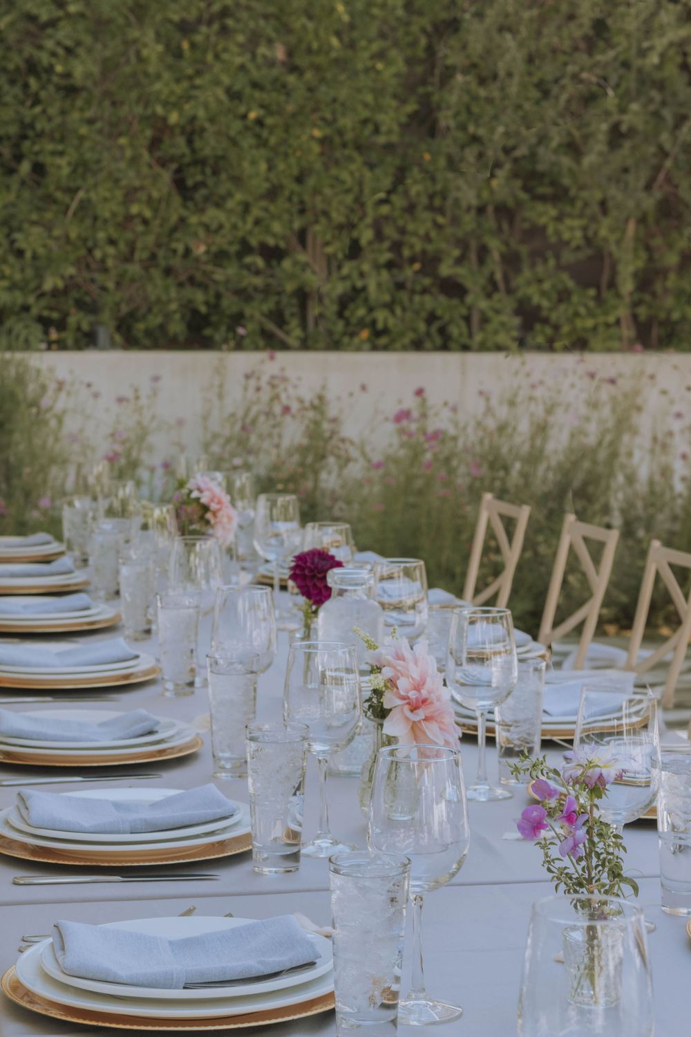Dining setup for wedding reception lined with flowers such as dahlias in clear, minimalist bottles.