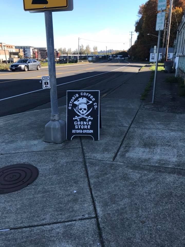 Black and white skull and crossbones sign on sidewalk near street pole.