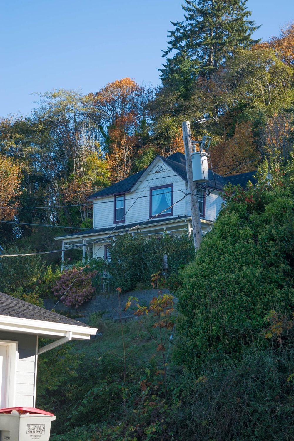 White hillside house with blue trim nestled among autumn trees.