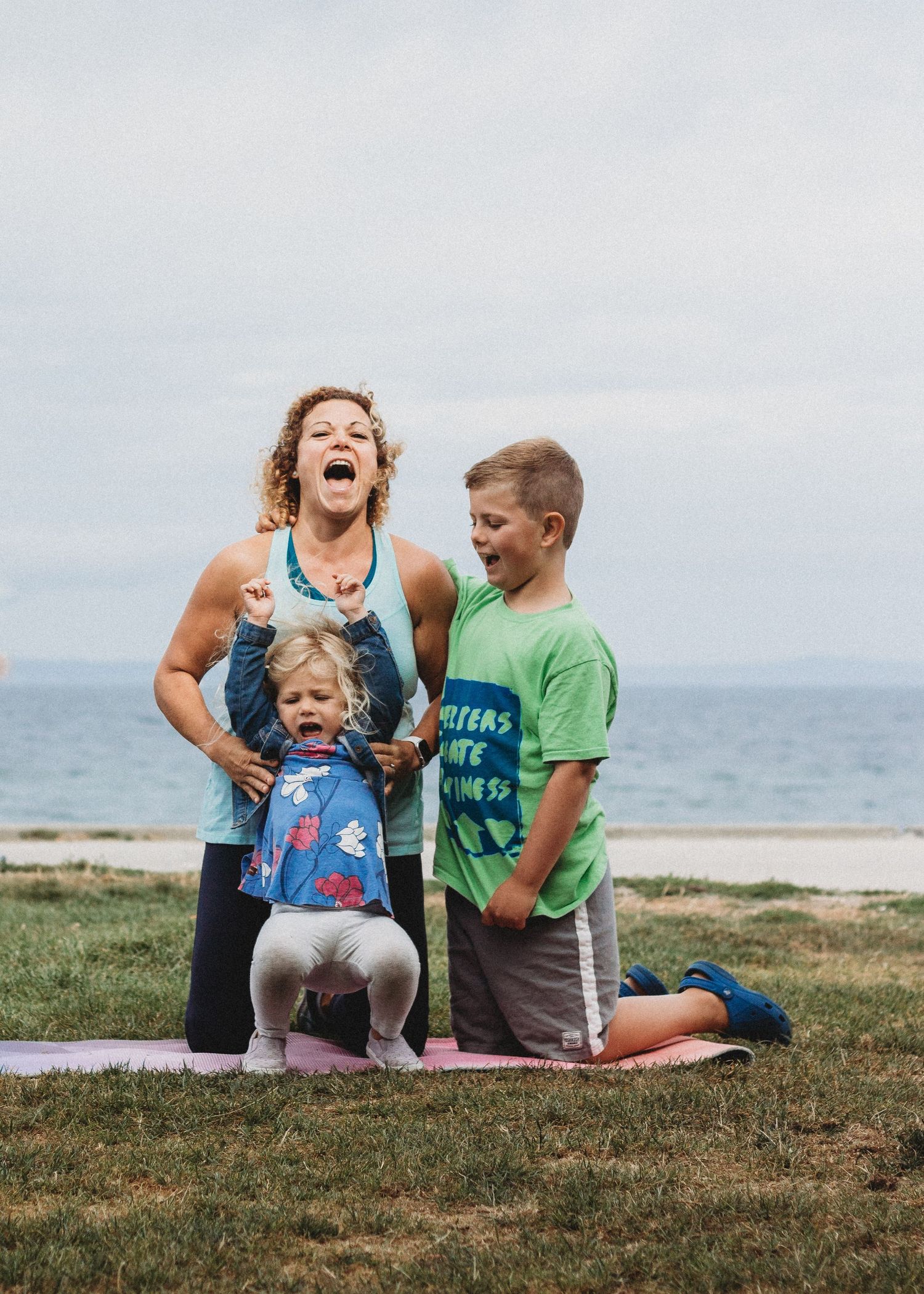 An energetic outdoor family moment on grass near the ocean.